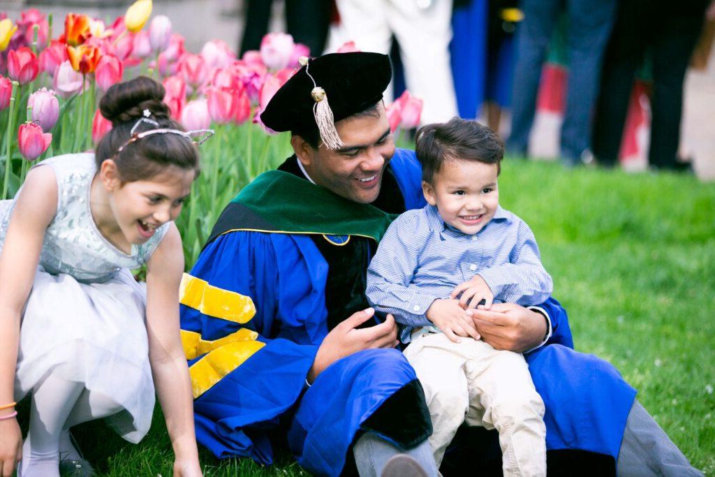 罗彻斯特大学的一名毕业生身着全套礼服，与他年幼的孩子们一起庆祝